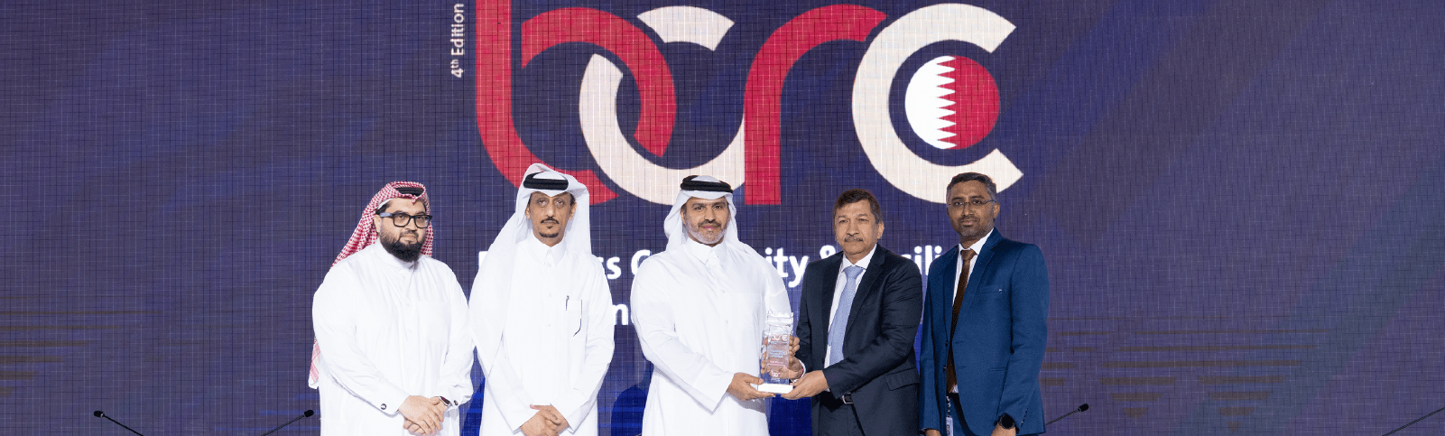Award handover scene with multiple participants standing in front of an event backdrop.